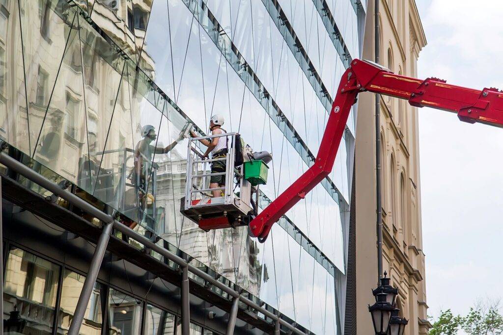 Arbeiter auf einer erhöhten Arbeitsplattform bei der Reinigung von Fensterglas an einer Gebäudefassade mit Hilfe von Werkzeugen zur Reinigung der verschmutzten Oberfläche. Selektiver Fokus