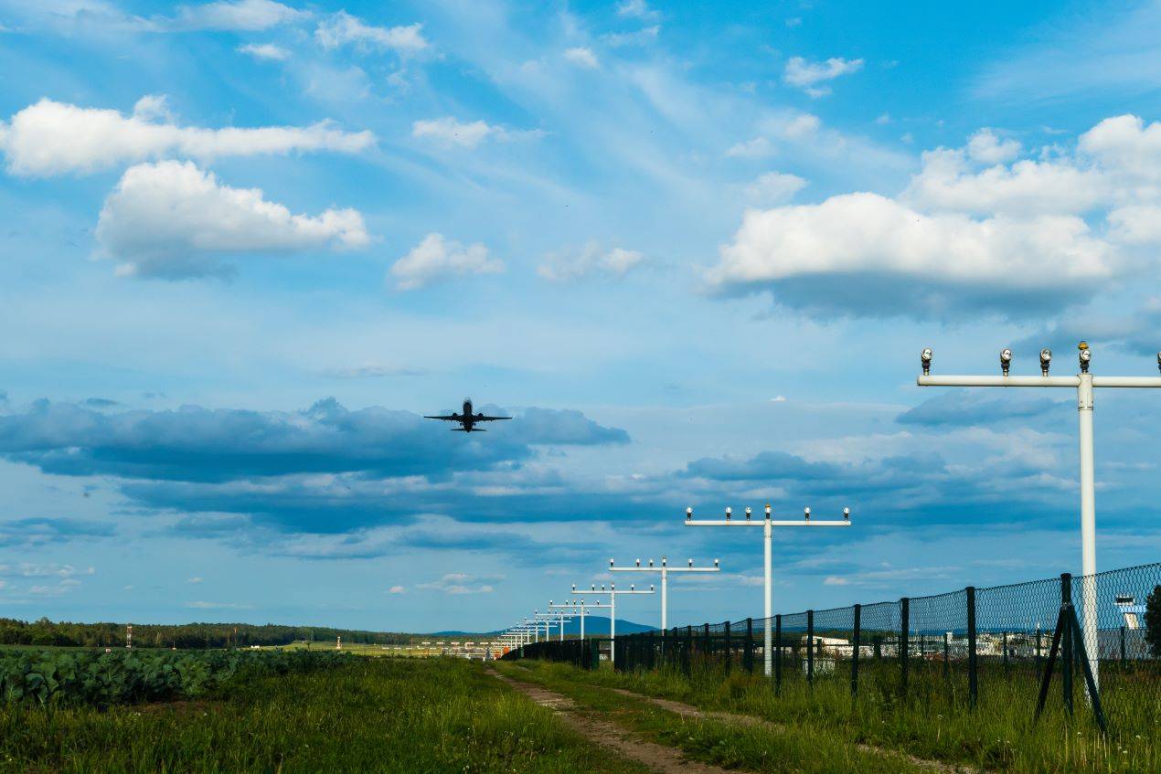 Ein Flugzeug hebt vom Flughafen Nürnberg ab, während es über eine grüne Wiese fliegt, umgeben von blauen Wolken und Startbahnlichtern