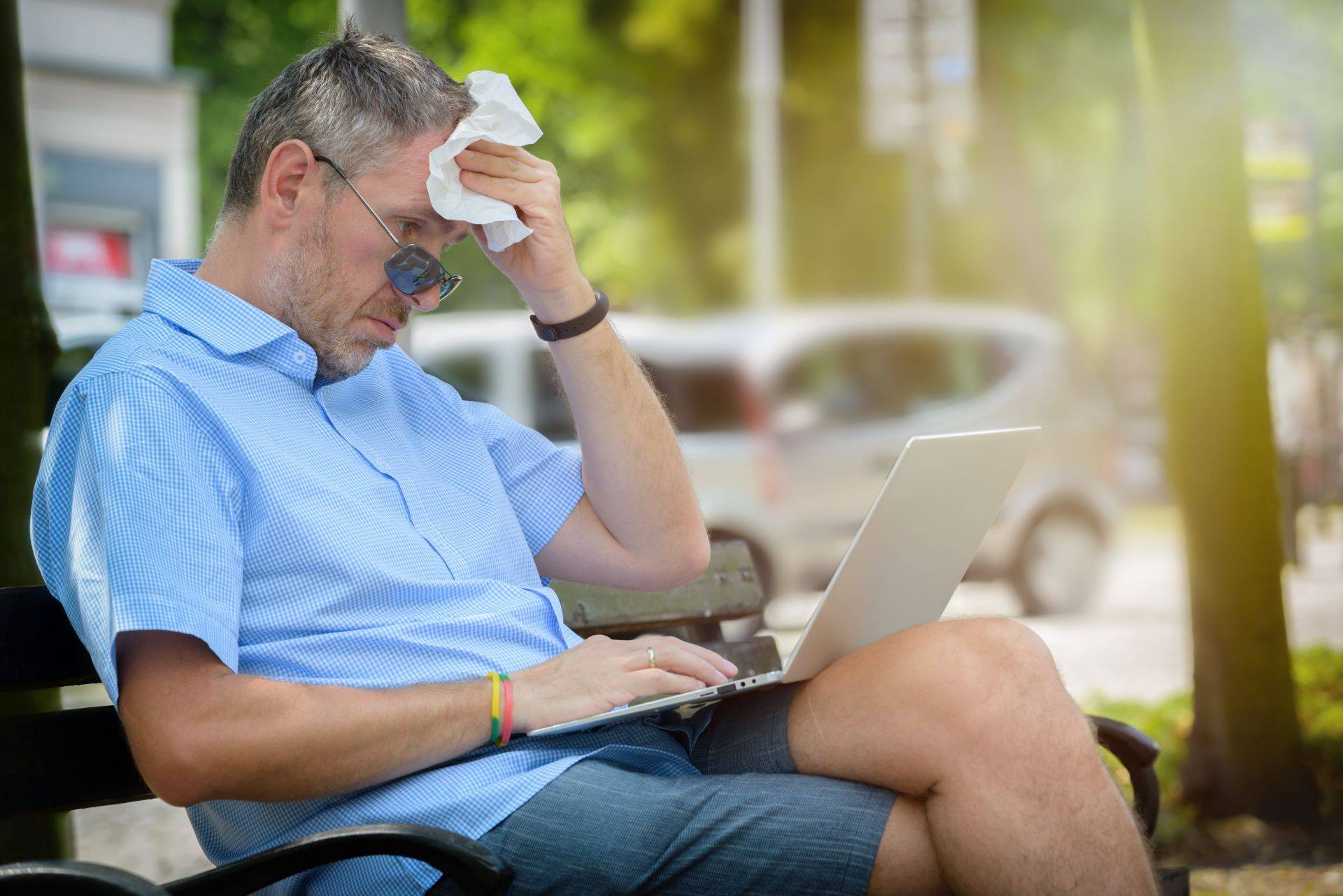 Mann mit Laptop im Park bei sommerlicher Hitze